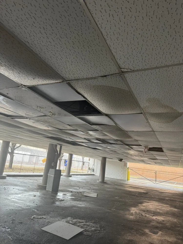 A parking garage ceiling with several water-stained and missing tiles exposes pipes and structure above, indicating a need for professional home repair and restoration service.